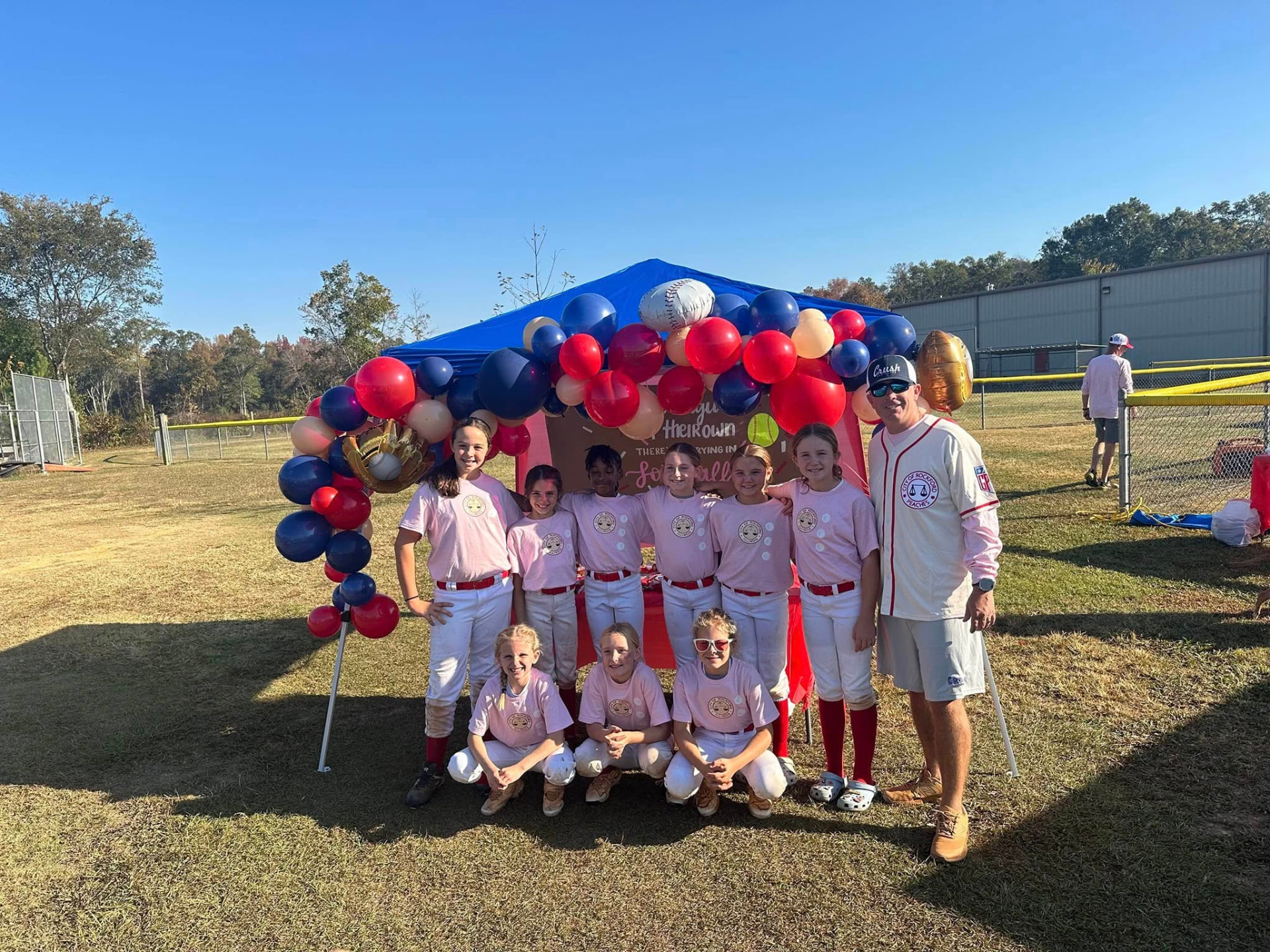 Team under a tent with red, white, and navy balloons